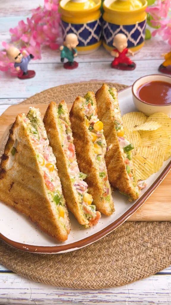 Toasted veg mayonnaise sandwich triangles with colourful vegetable filling, served with potato chips and ketchup